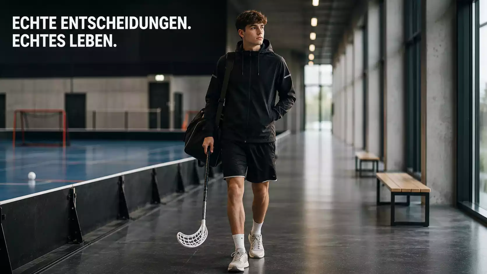 Jugendlicher mit Smartphone sitzt auf einer Bank vor einer Sporthalle