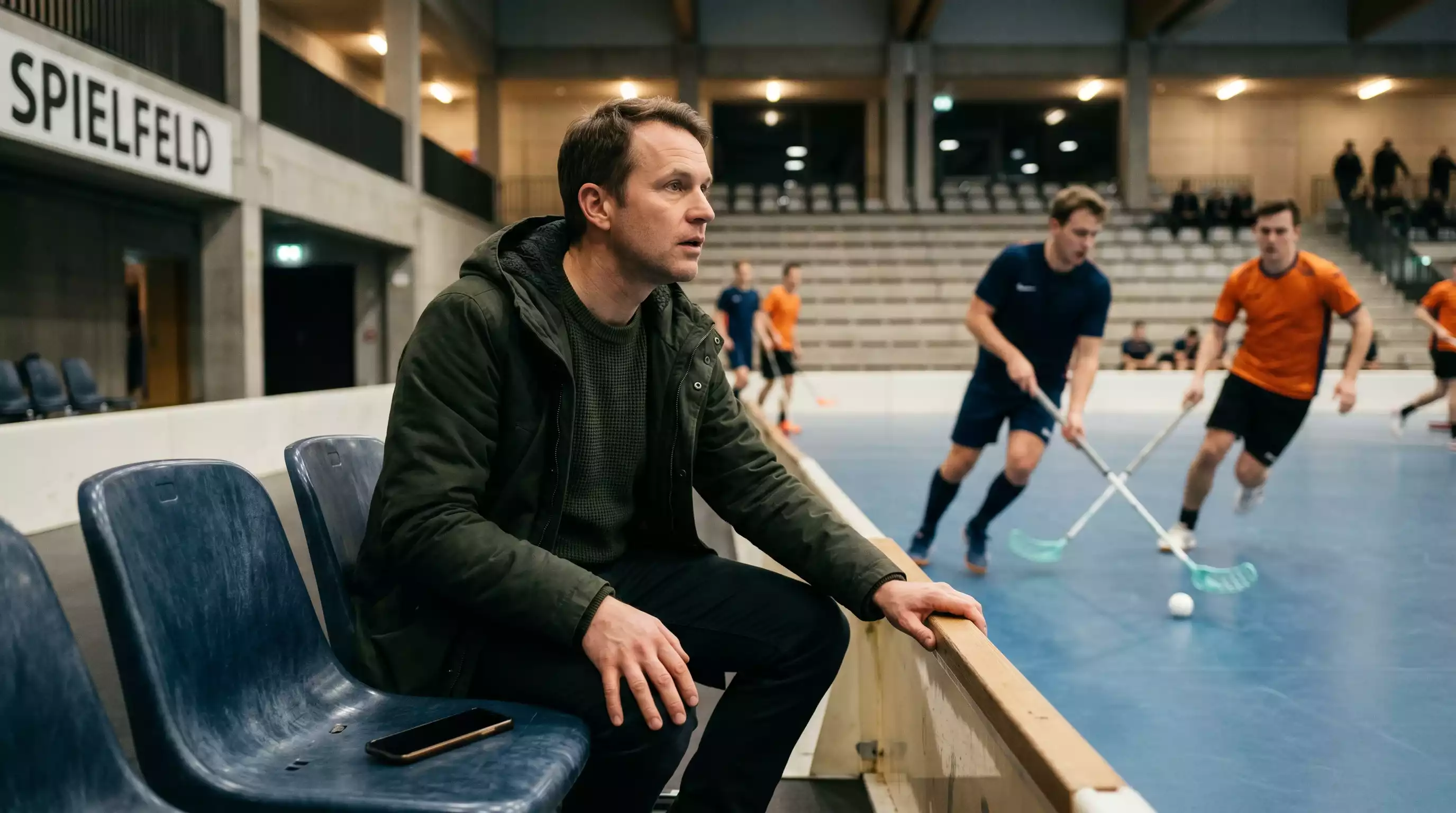 Wettender platziert konzentriert eine Live-Wette am Mobilgerät am Spielfeldrand einer Unihockey-Halle