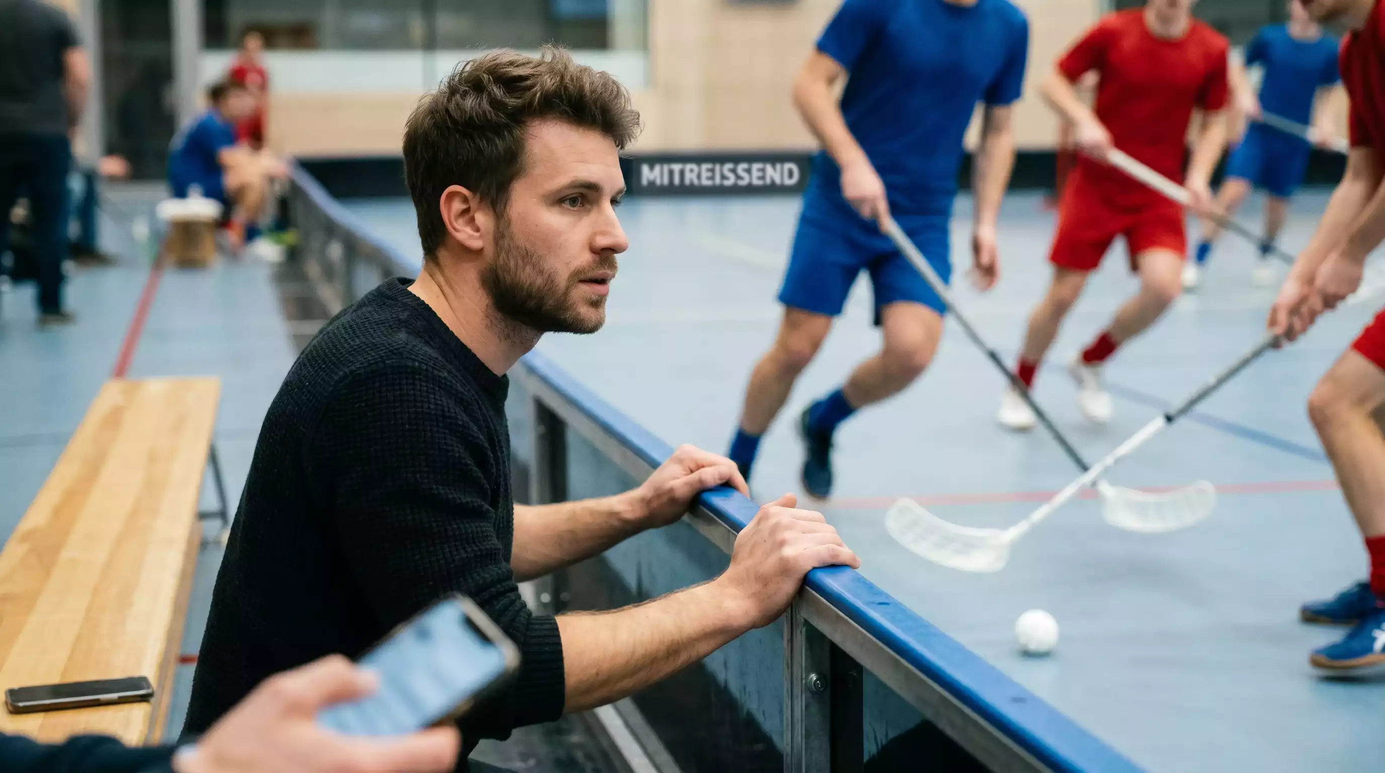 Unihockey-Spieler platziert eine Live-Wette am Smartphone während eines laufenden Floorball-Spiels